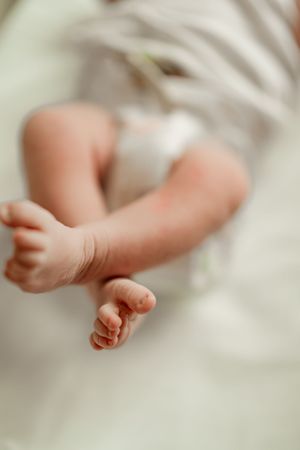 Soft focus close-up of delicate newborn baby legs and tiny feet resting on a white blanket.