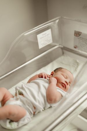 Newborn baby sleeping in hospital bassinet wearing white outfit after delivery.