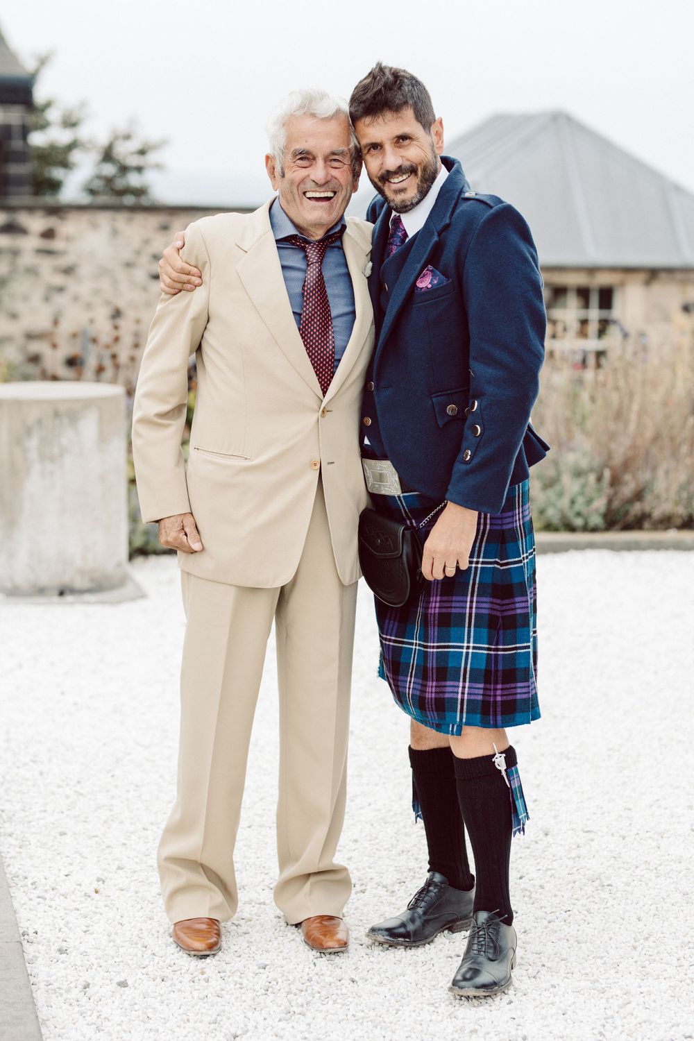 Two people in formal wear share candid moments on white gravel surface.