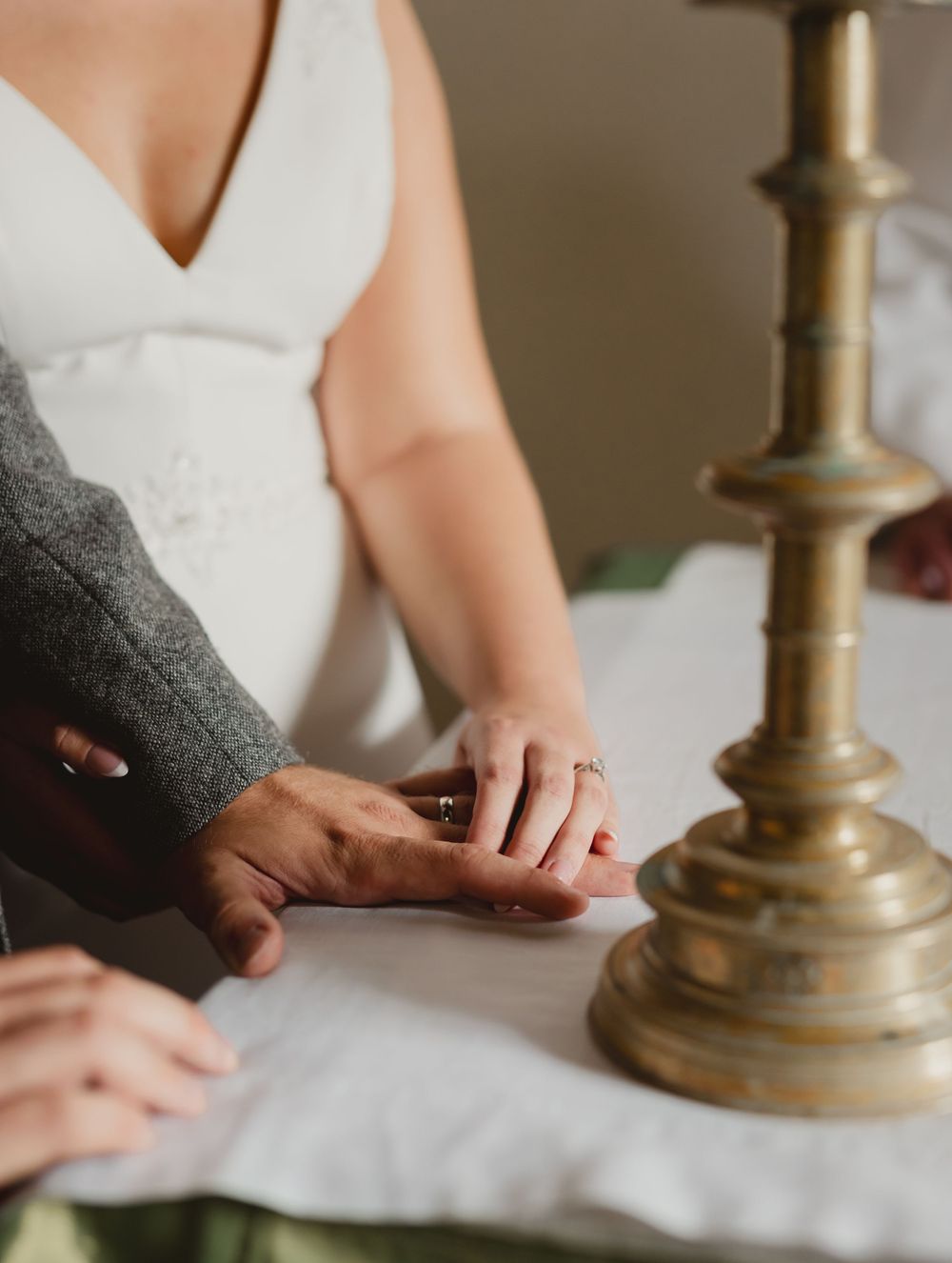 Close-up of hands arranging elegant brass candlesticks on white tablecloth.
