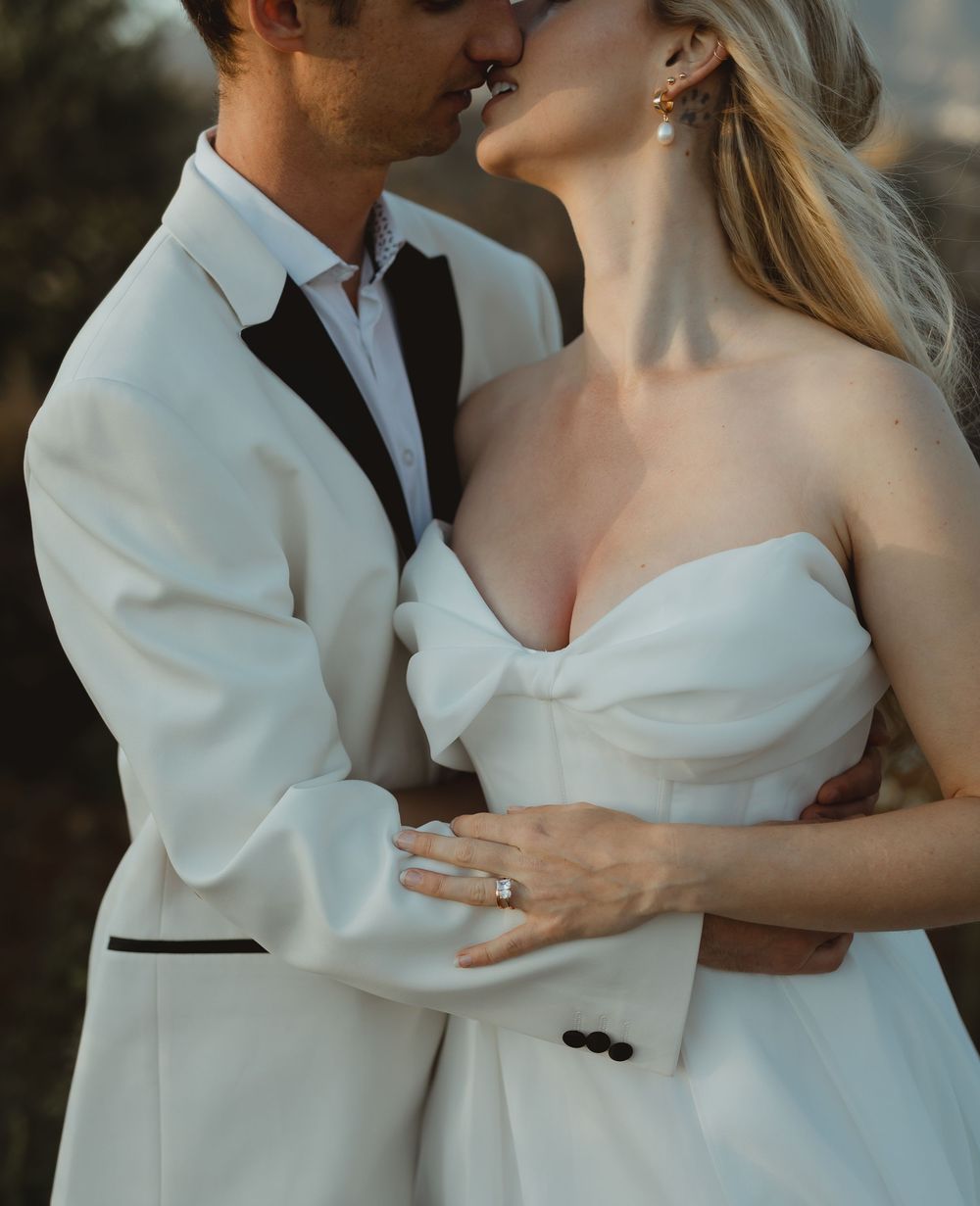 Romantic wedding portrait showing couple in white formal attire embracing during an intimate moment at sunset.