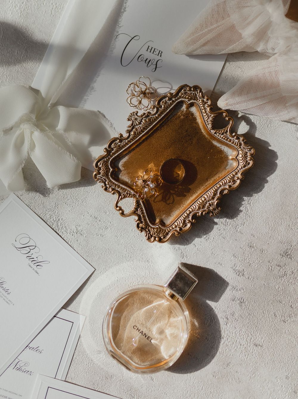 Elegant golden wax seal and ornate antique frame with delicate wedding stationery on a textured white surface.