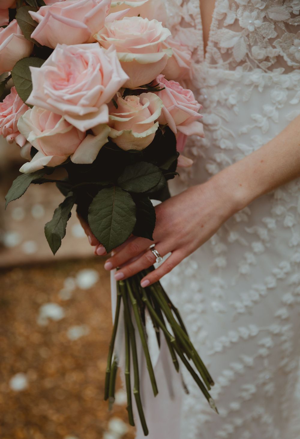 Elegant bouquet of pale pink roses held against textured white wedding dress.