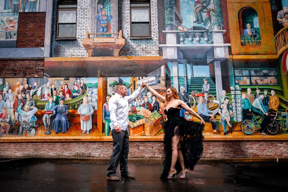A couple poses in front of colorful street art murals in an urban setting.