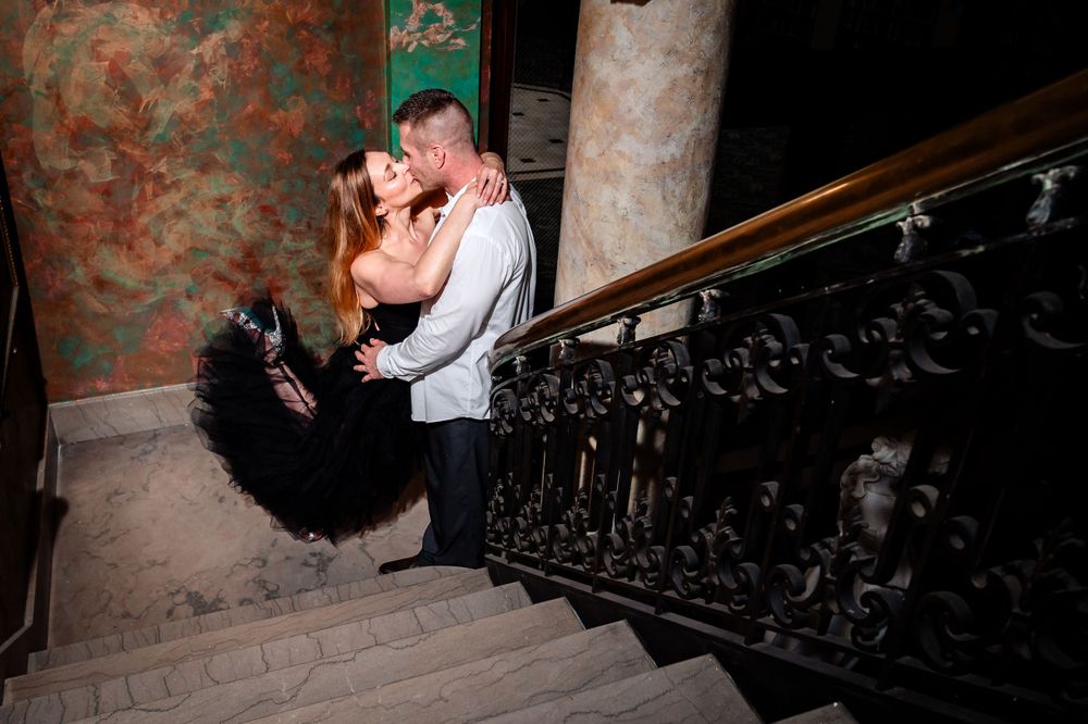 A couple shares an intimate moment on vintage stairs with ornate iron railings.