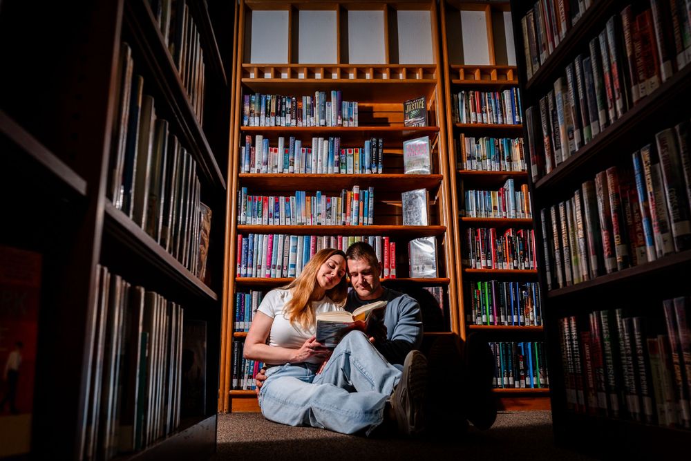 A romantic engagement photo session in a library with bookshelves creating a cozy backdrop.