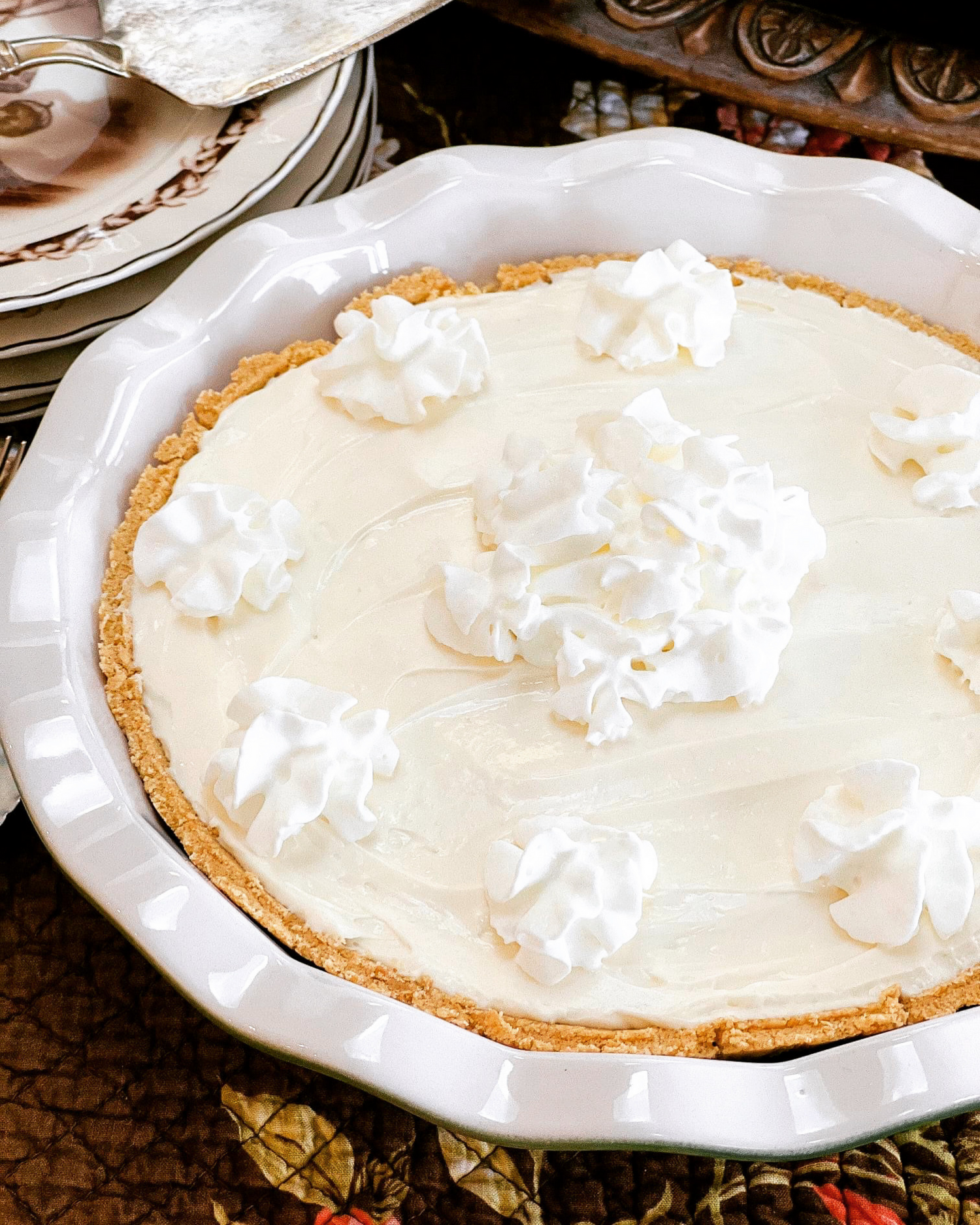 Homemade cream pie with whipped cream dollops in white ceramic pie plate.