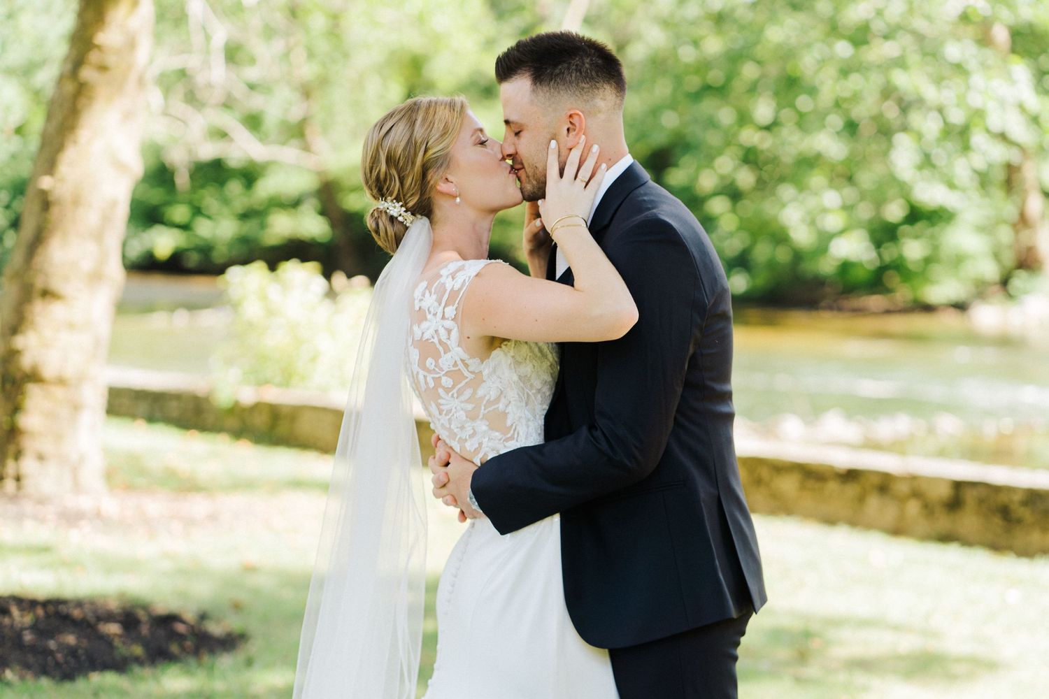 Romantic wedding couple sharing an intimate kiss in a sunlit garden with lush greenery.
