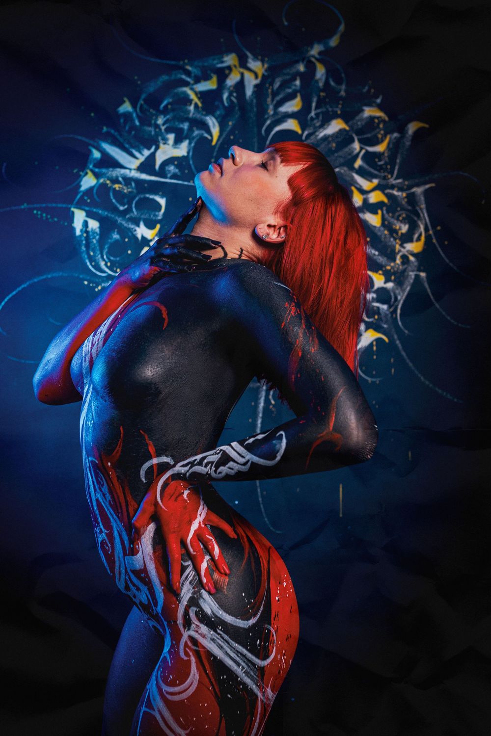 Woman with red hair covered in blue, red, and white body paint against decorative background.
