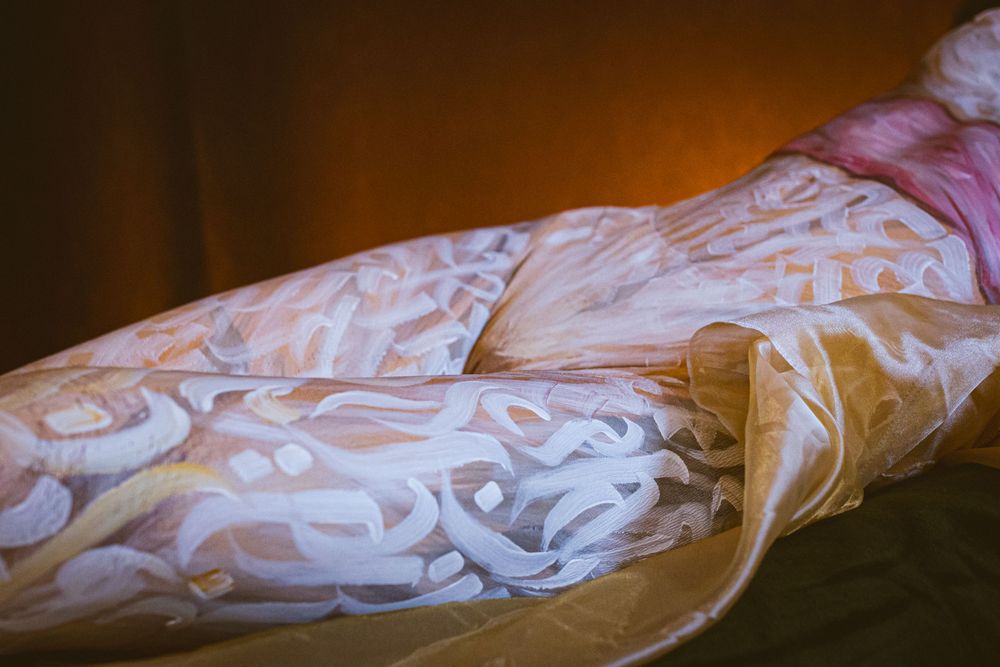 Close-up of an arm with intricate white Arabic calligraphy body art projected onto skin in warm amber light.