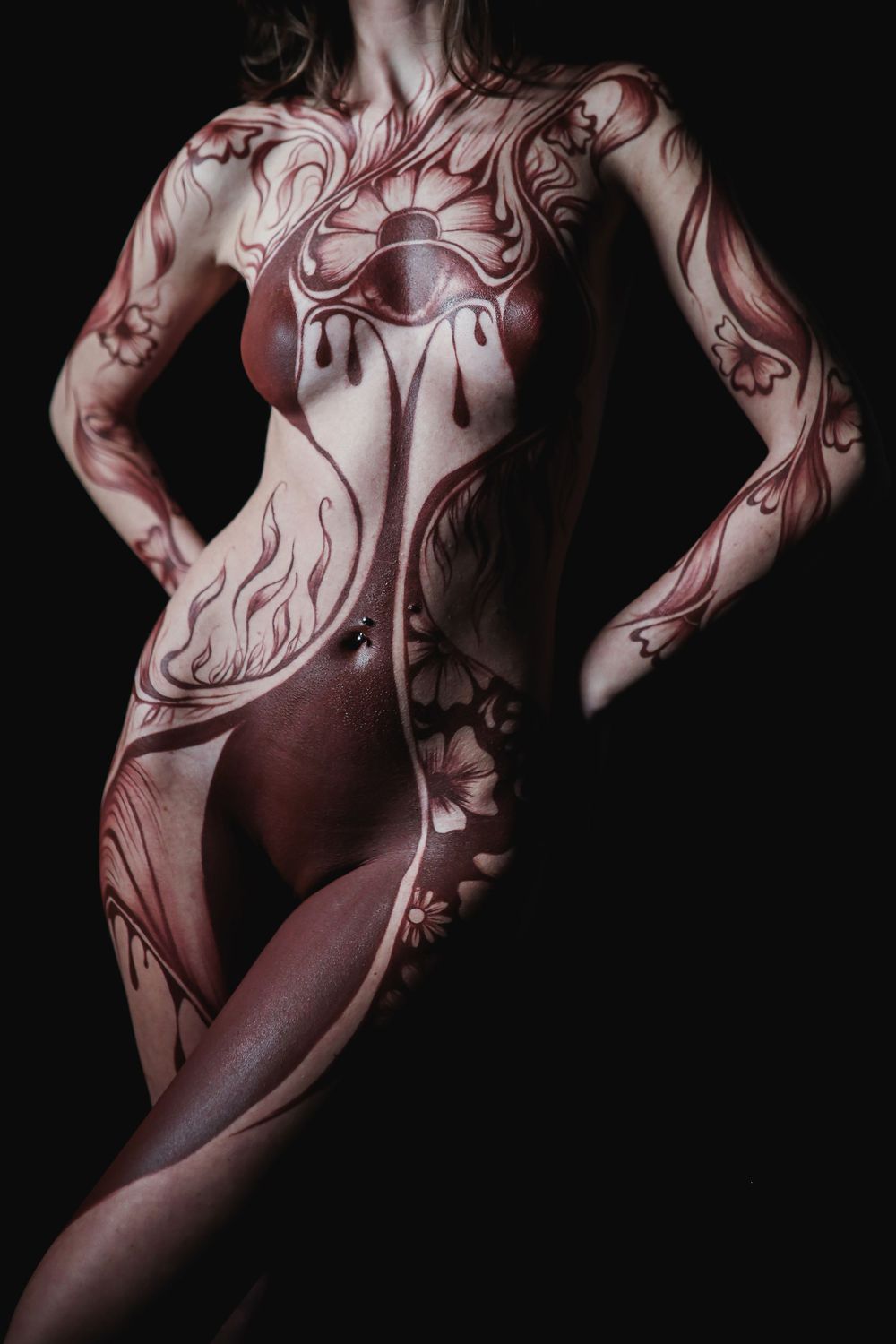 Artistic full body paint design in red and white floral motif on female figure against black background.