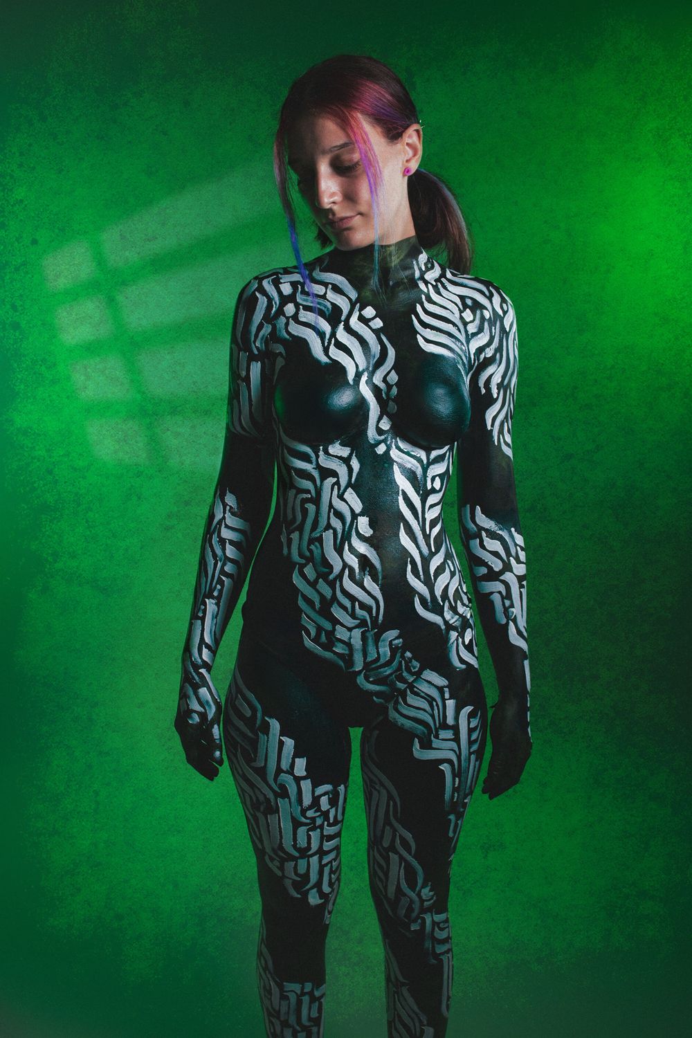 Woman with circuit board-inspired black and white body paint standing in green neon light.