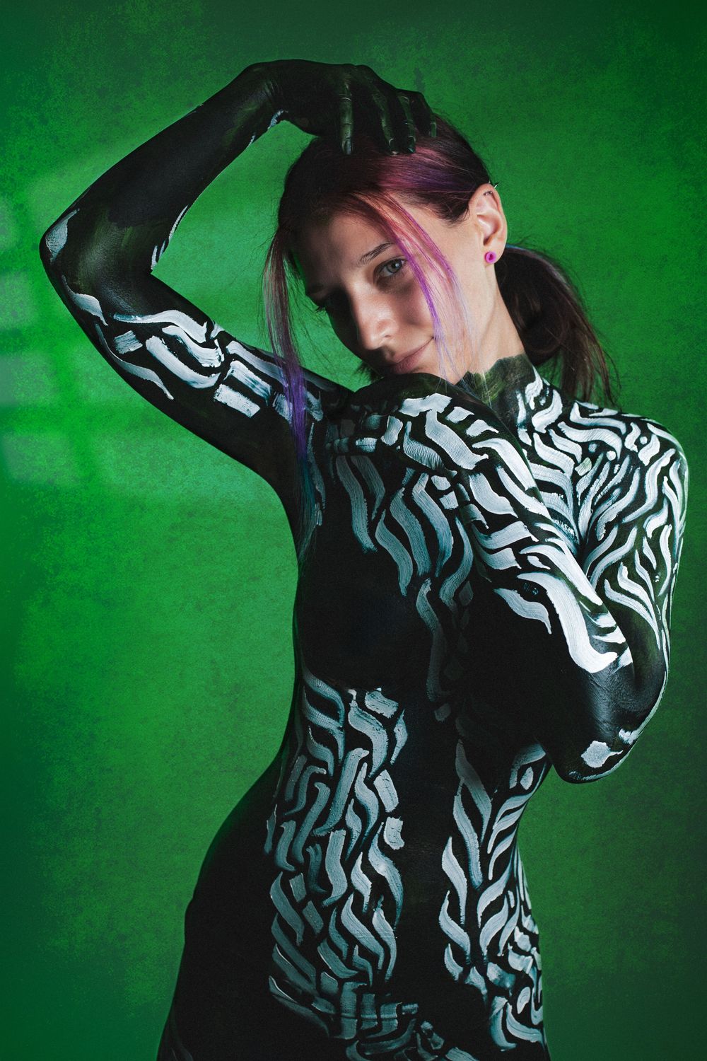 Model in black and white zebra body paint poses dramatically against green studio backdrop.