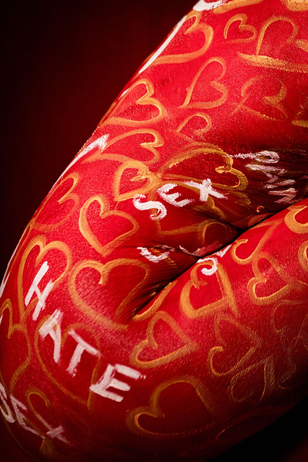 Close-up of red body paint with gold hearts and words like HATE and SEX on skin.