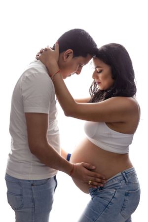Intimate maternity photo of couple in white and denim sharing tender moment.