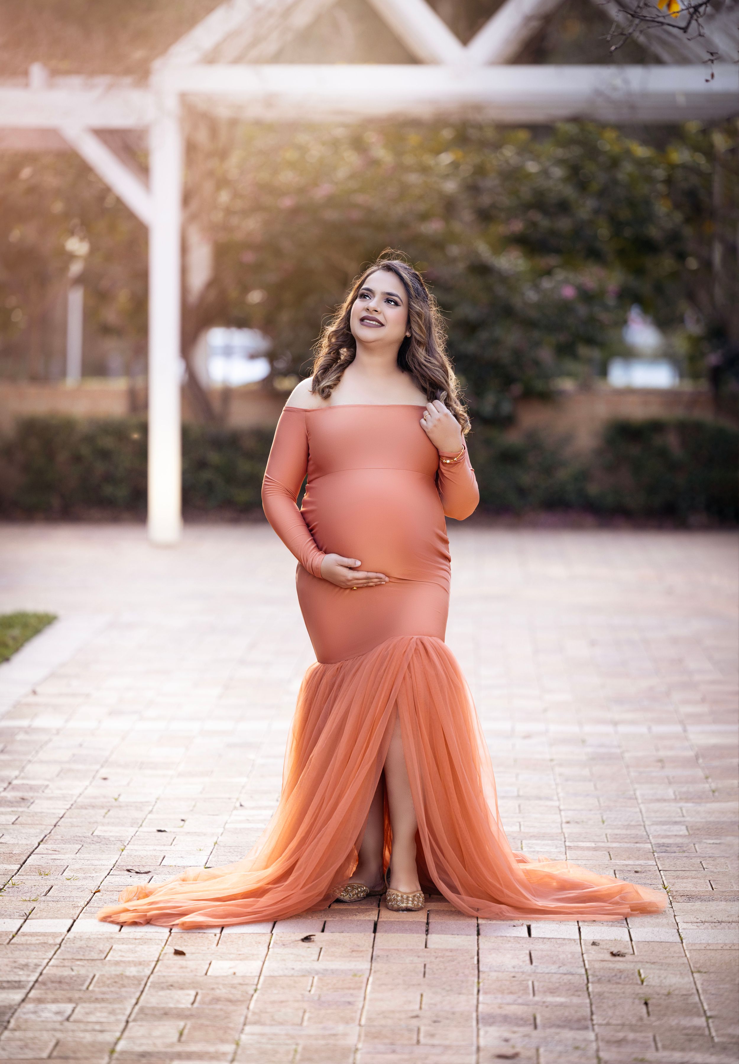 Maternity photo of expecting mother in flowing peach gown on brick pathway.