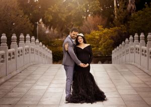Elegant maternity portrait of couple on stone bridge wearing formal attire.