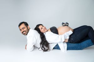 Playful maternity studio photo of couple in white shirts and jeans on white background.