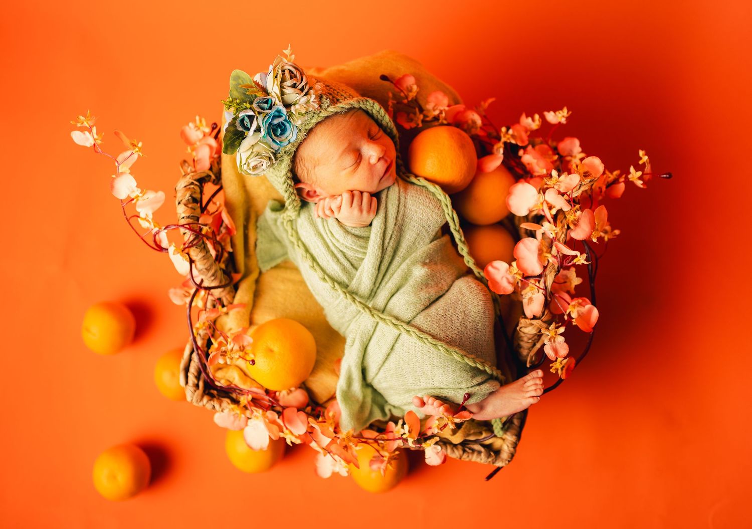 Neugeborenes Baby auf orangefarbenem Hintergrund mit Orangenfrucht-Dekoration, kreativ und frisch inszeniert