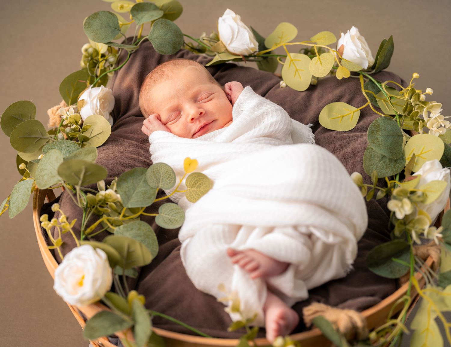 Neugeborenes Baby liegt auf einem runden Bett, hält seine Ohren und posiert in einer niedlichen und einzigartigen Haltung