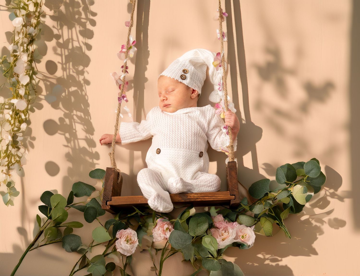 Neugeborenes Baby auf einer Schaukel mit Pflanzen dekoriert, kreativ und liebevoll für ein einzigartiges Fotoshooting arrangiert