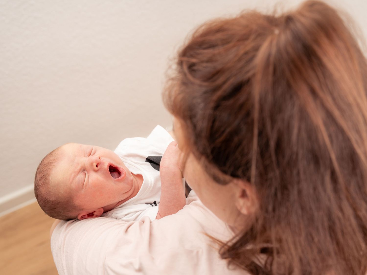 1 Monat altes Baby gähnt in den Armen der Mutter, eine liebevolle und natürliche Momentaufnahme