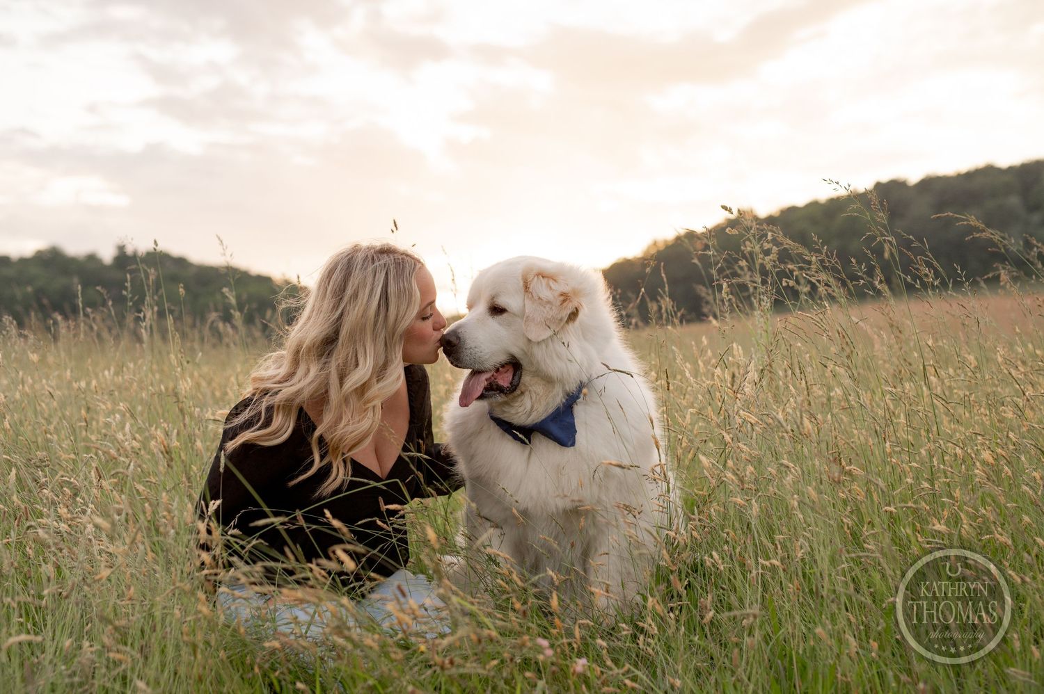 A sweet moment captured between a fluffy white dog and someone in a black sweater in a field.