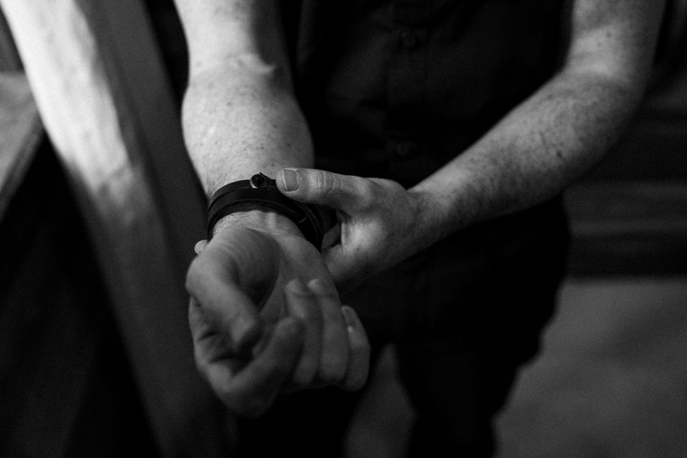 Close-up black and white photo of hands adjusting a watch in dim lighting.