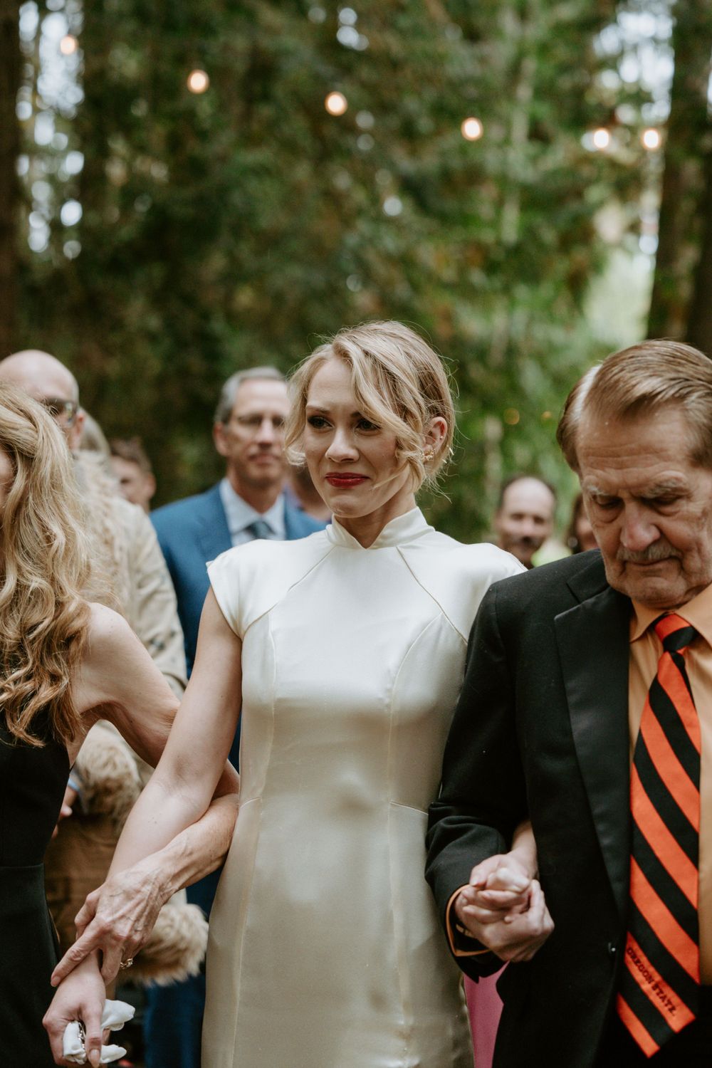 Wedding guests gather around the couple during an outdoor forest celebration.