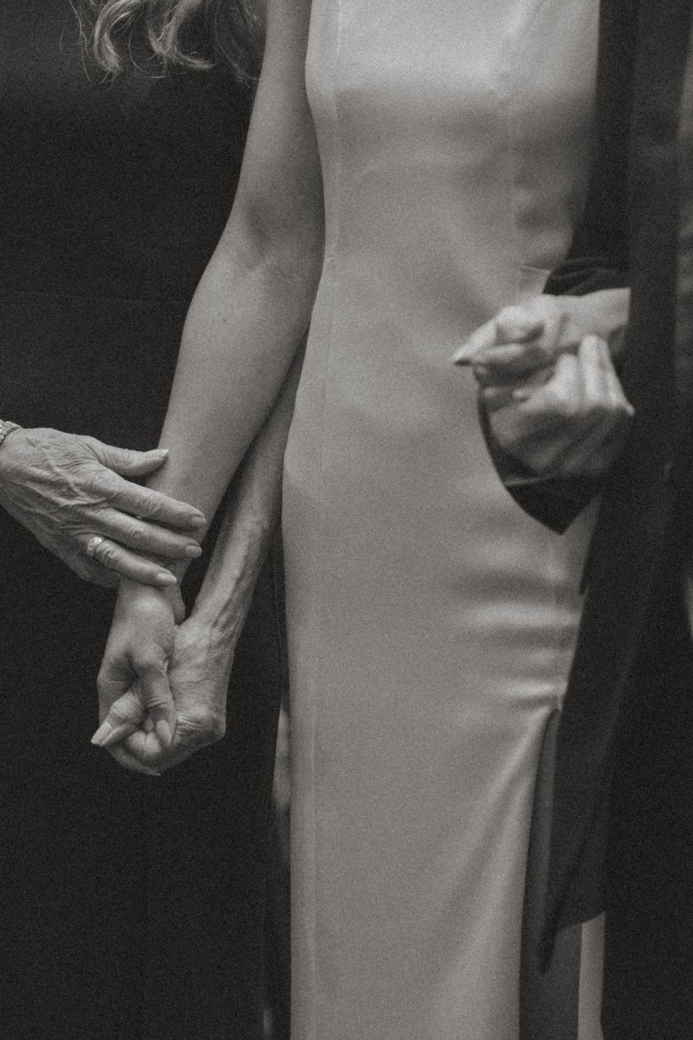 Artistic black and white detail of a sleek white wedding dress and gentle hand placement.