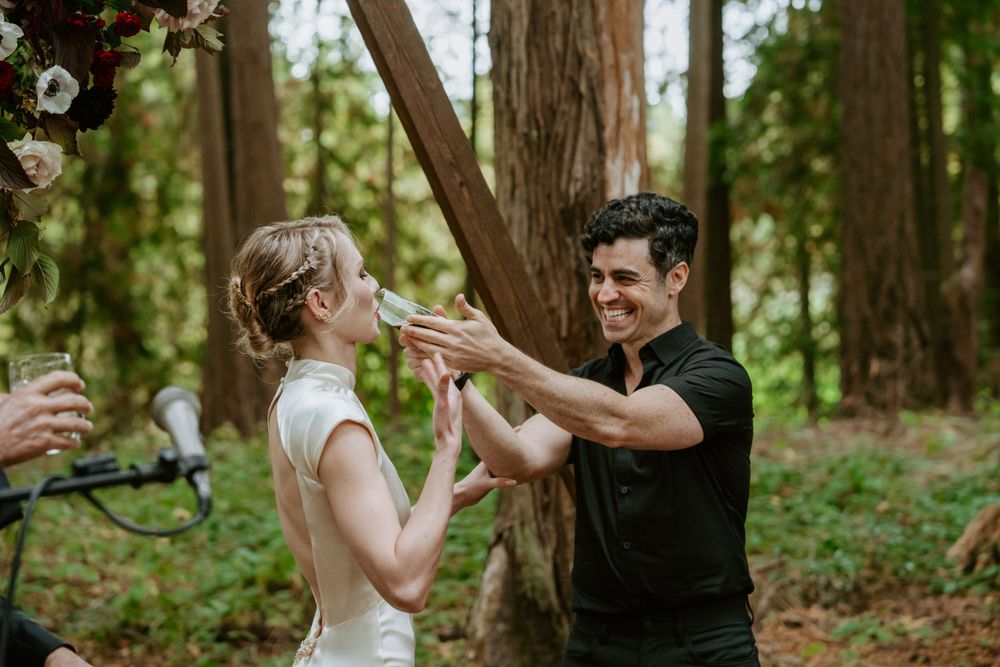 Couple sharing a celebratory champagne toast in a forest wedding setting.