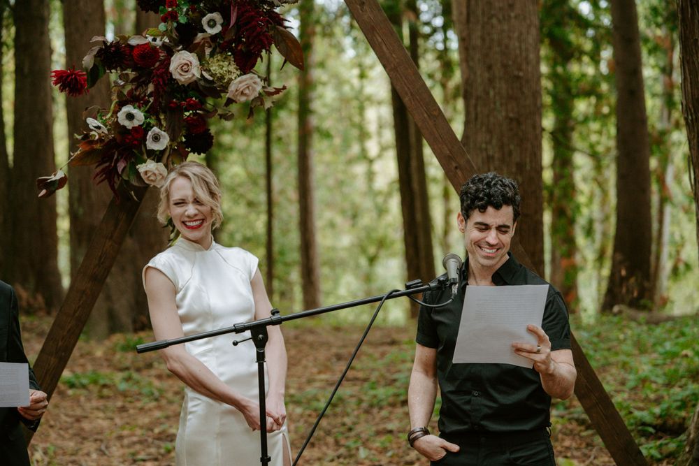 Wedding ceremony with floral arrangements and microphones in a forest setting.