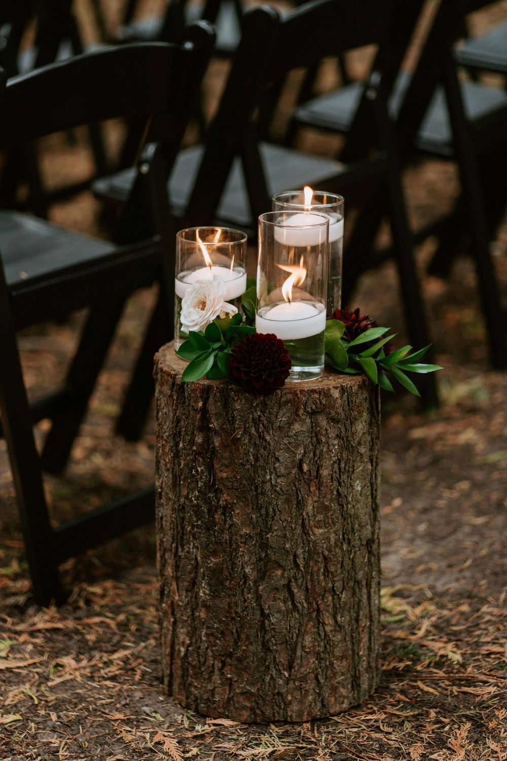 Rustic wedding decor featuring floating candles on a tree stump with greenery and flowers.