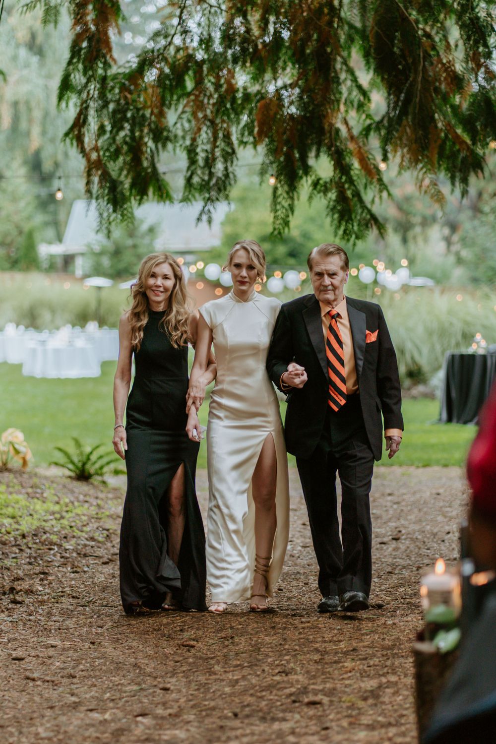 Wedding processional along a forest path with formal attire and natural scenery.