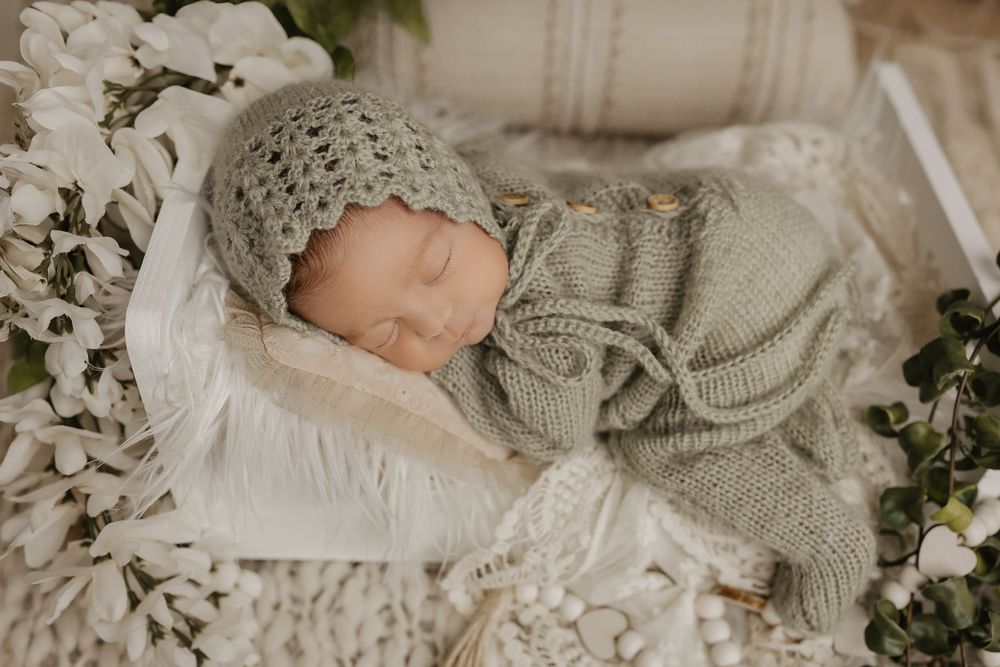 Newborn resting on white blanket surrounded by delicate floral arrangements and greenery.