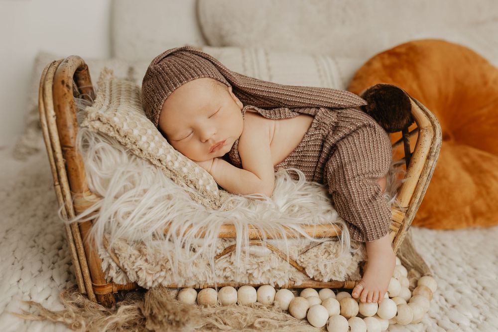 Sleeping newborn in brown outfit nestled in rustic wooden basket.