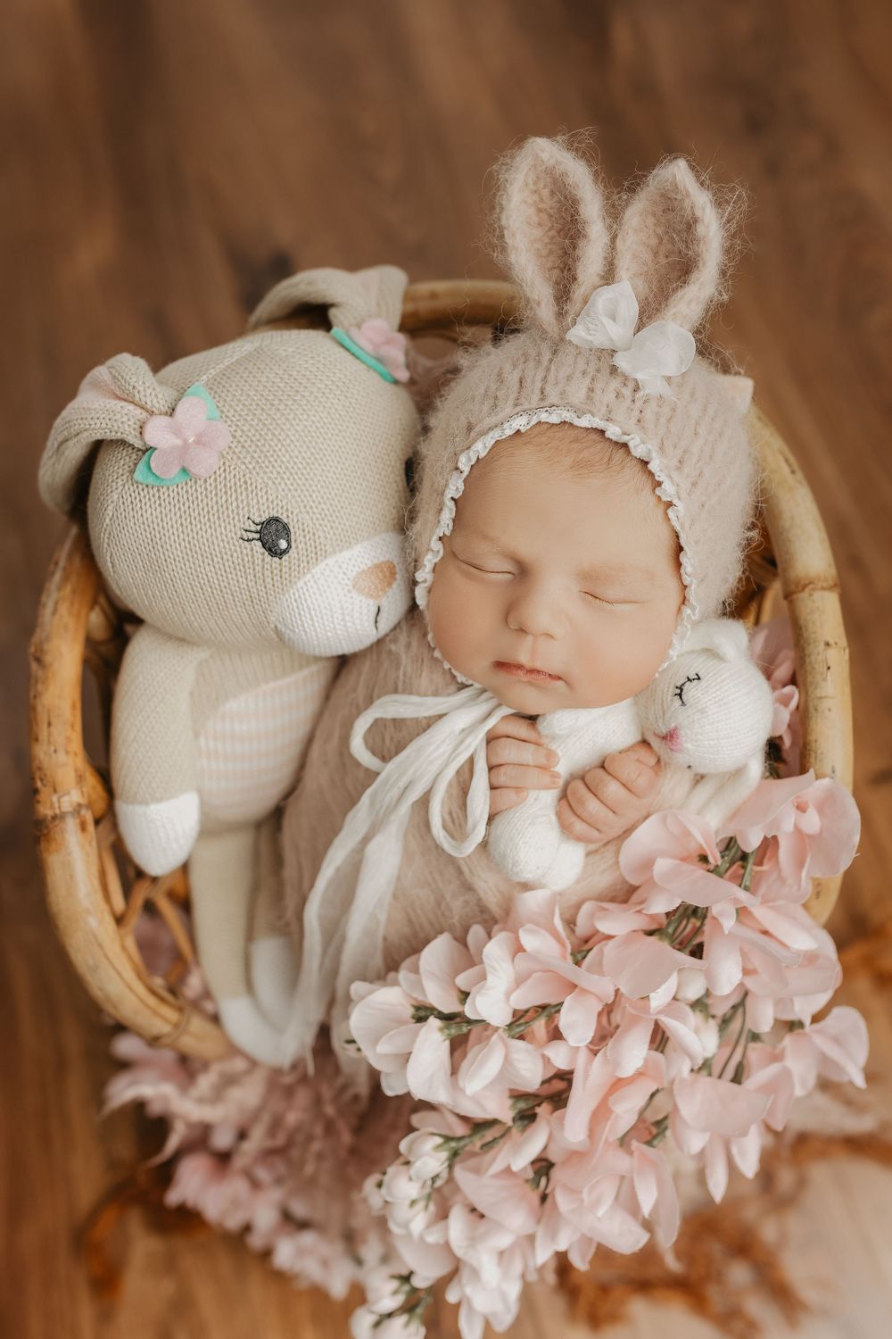 Sleeping baby surrounded by plush bunny toys and pink floral decorations.