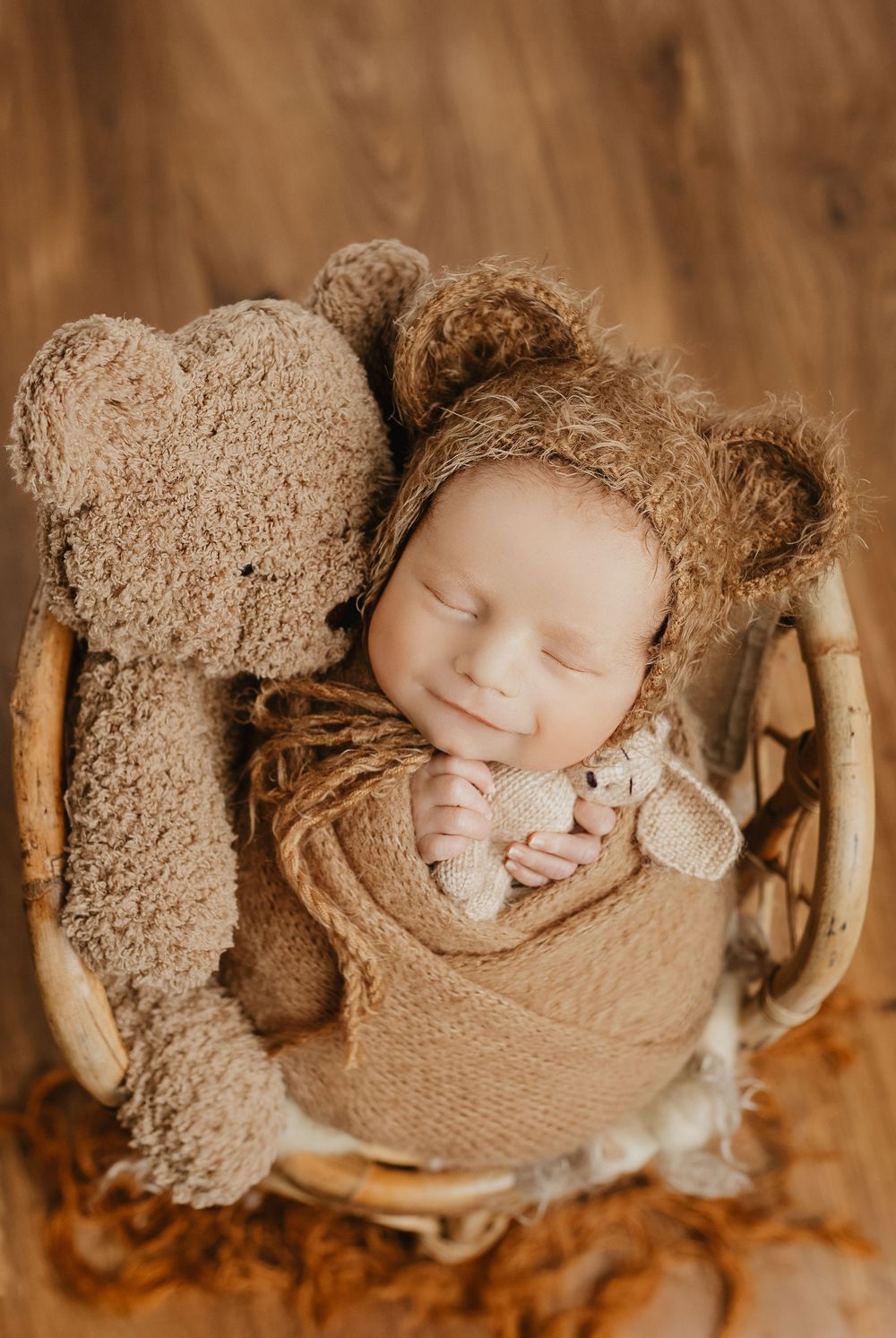 Newborn sleeping in rustic wooden bowl with textured beige blanket.