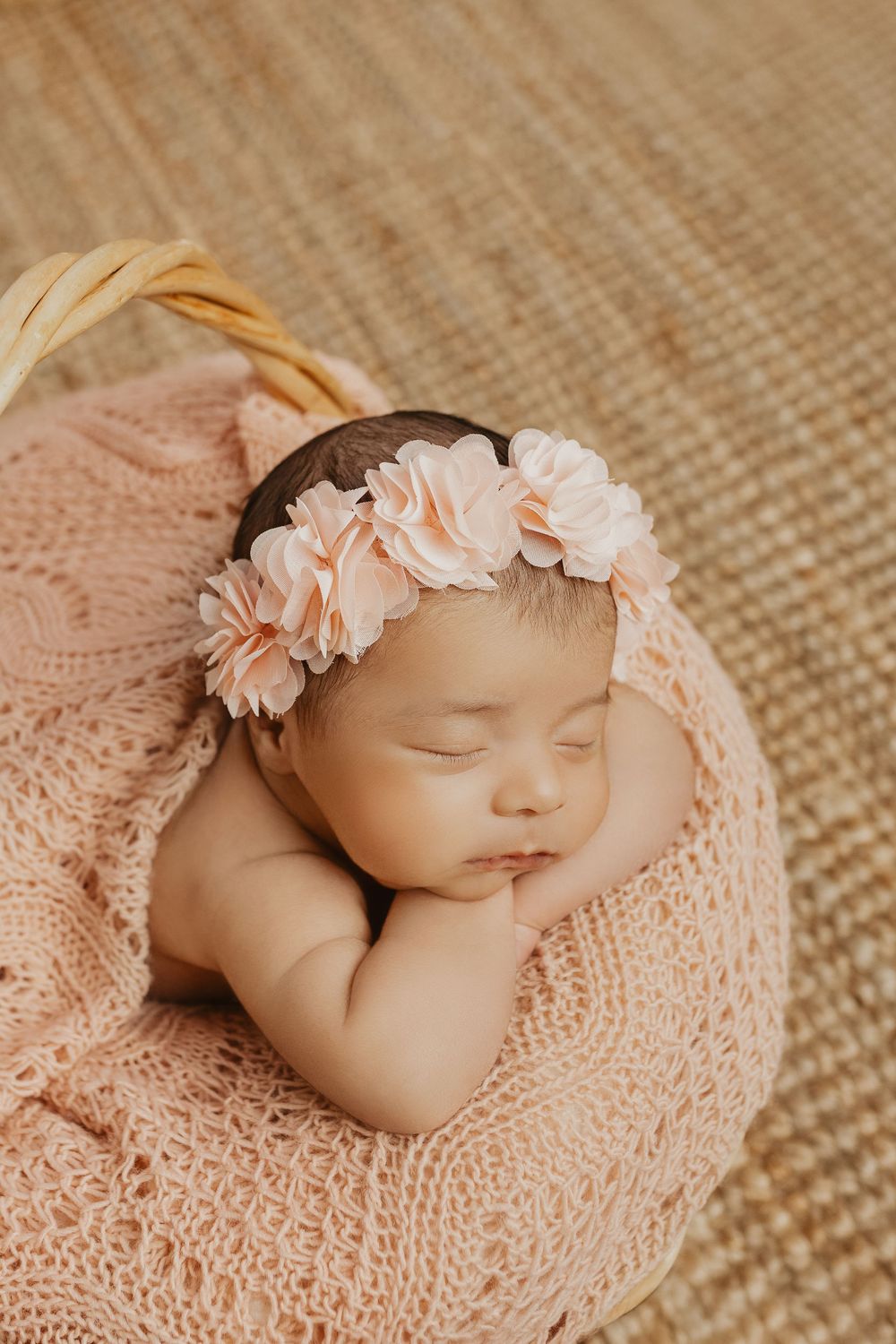 Sleeping newborn wrapped in soft pink knit blanket with delicate floral headband.