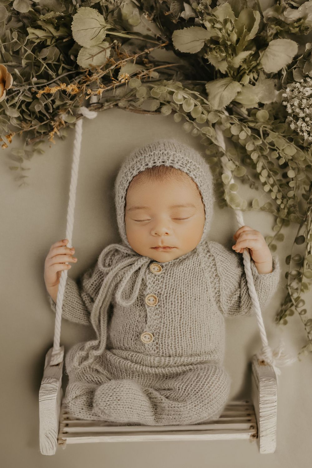 Peaceful newborn resting on white swing wearing cozy gray knitted outfit.