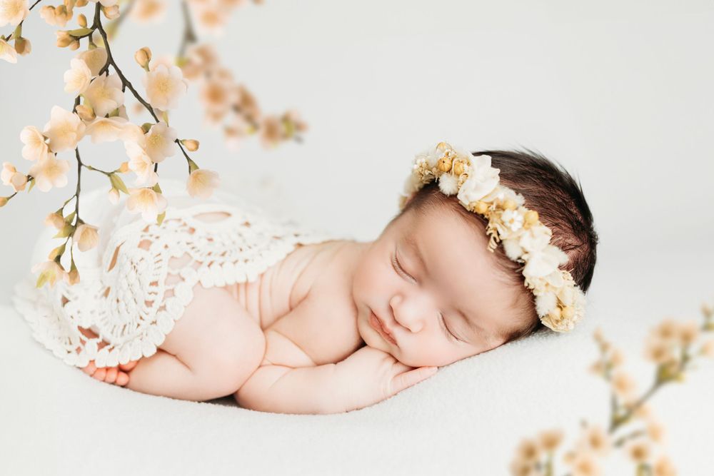 Newborn baby sleeping peacefully with peach floral decorations on white background.
