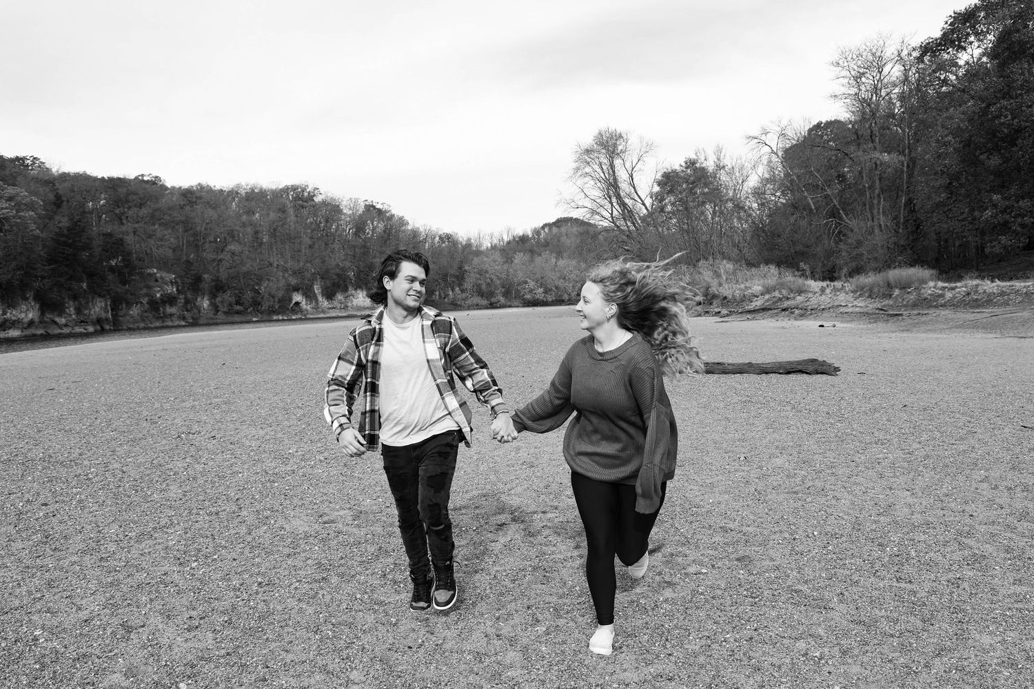 Couple walking together and holding hands in a wide open field on an overcast day.