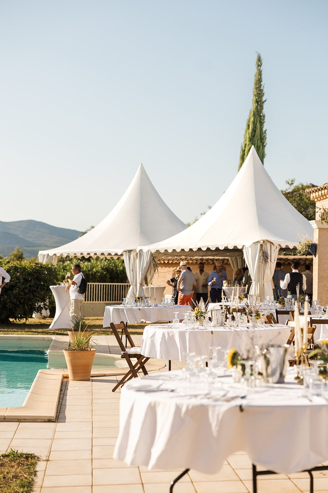 White canopy tents and elegant table settings arranged for an outdoor event beside a waterfront terrace.