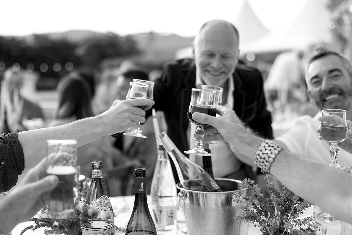 People celebrating and toasting with wine glasses at an outdoor gathering in black and white.