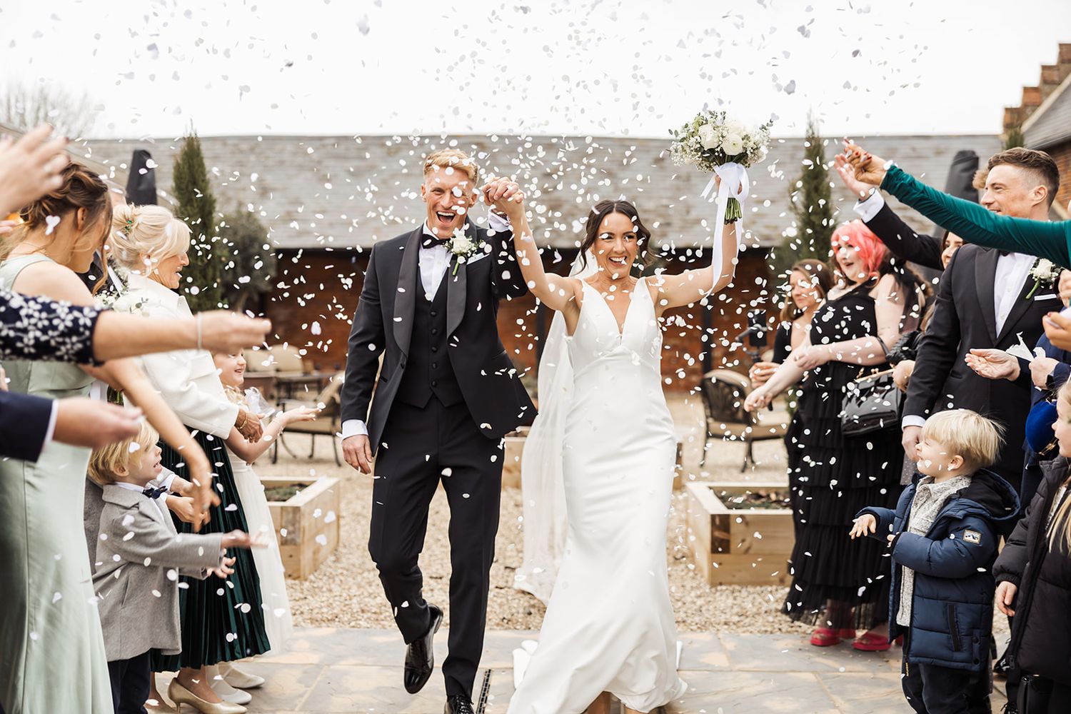 A celebratory wedding exit with guests throwing confetti as the newlyweds walk through with joyful expressions.