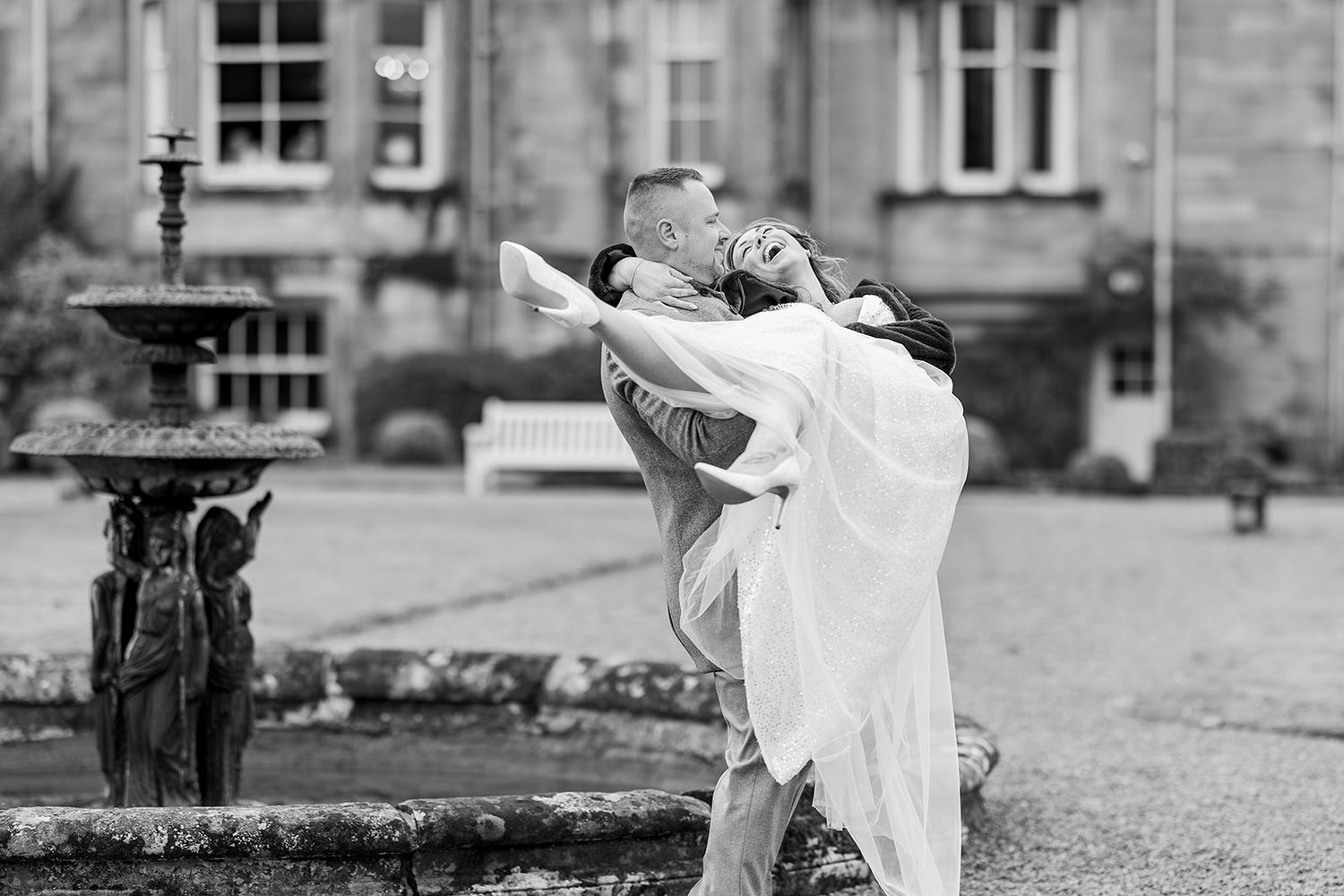 Couple in romantic embrace with person in white dress being lifted and dipped during outdoor celebration.