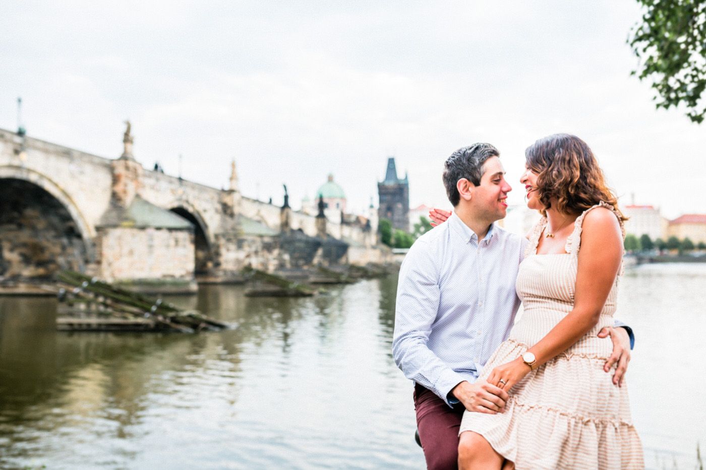 Romantic couple by Charles Bridge in Prague with historic architecture in the background.