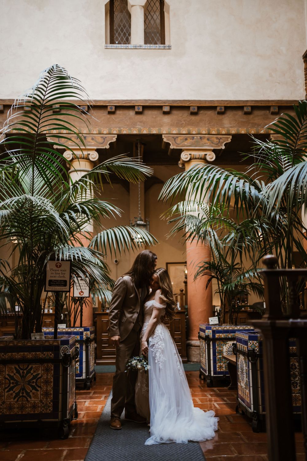 A romantic wedding photo amid palm trees in a Spanish-style courtyard.