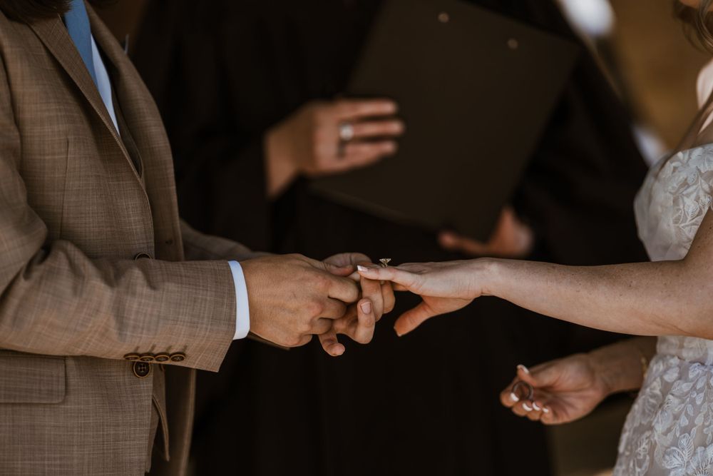 A close-up of hands exchanging rings during an outdoor wedding ceremony.