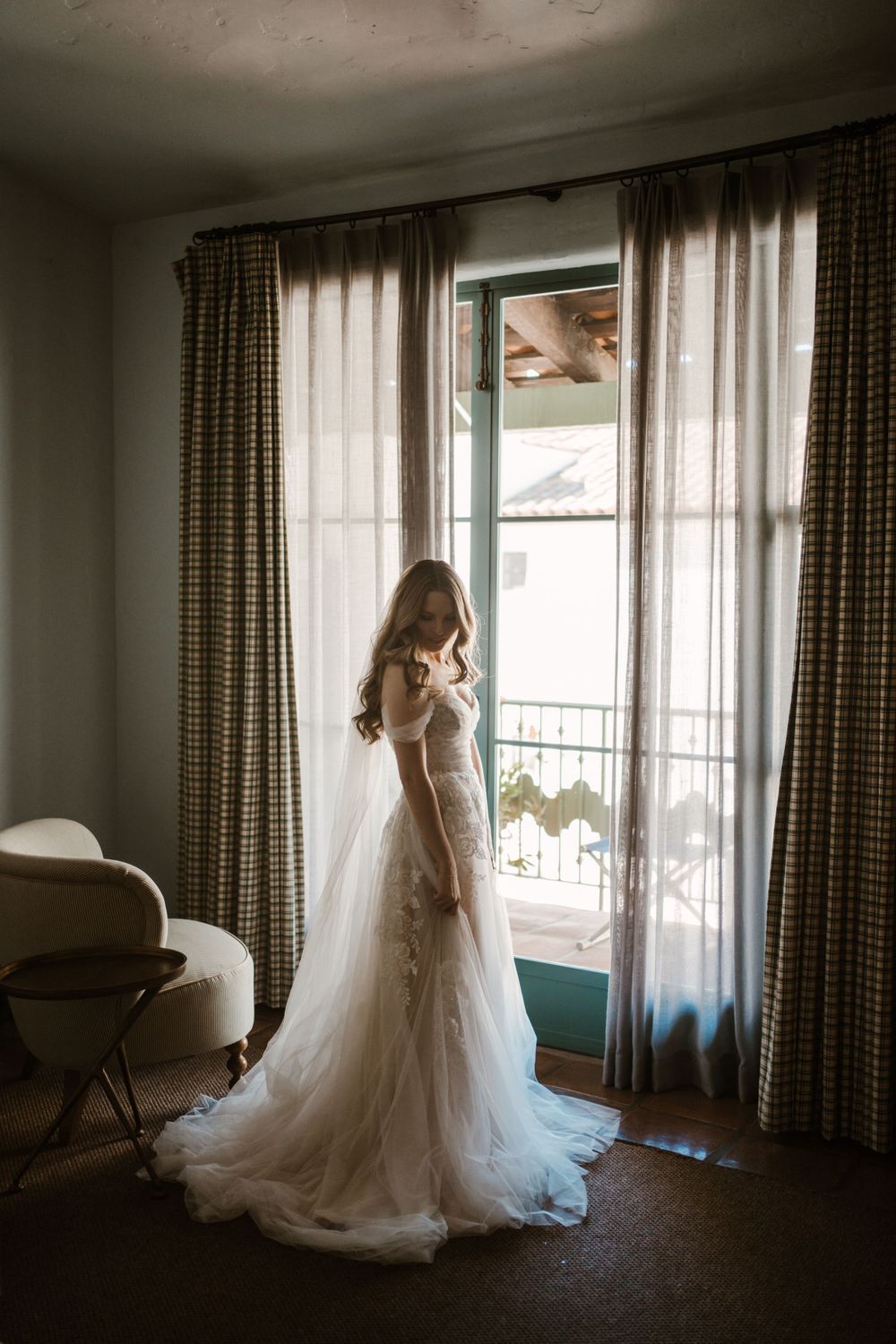 A silhouette of someone in a wedding dress standing by a window with classic checkered curtains.